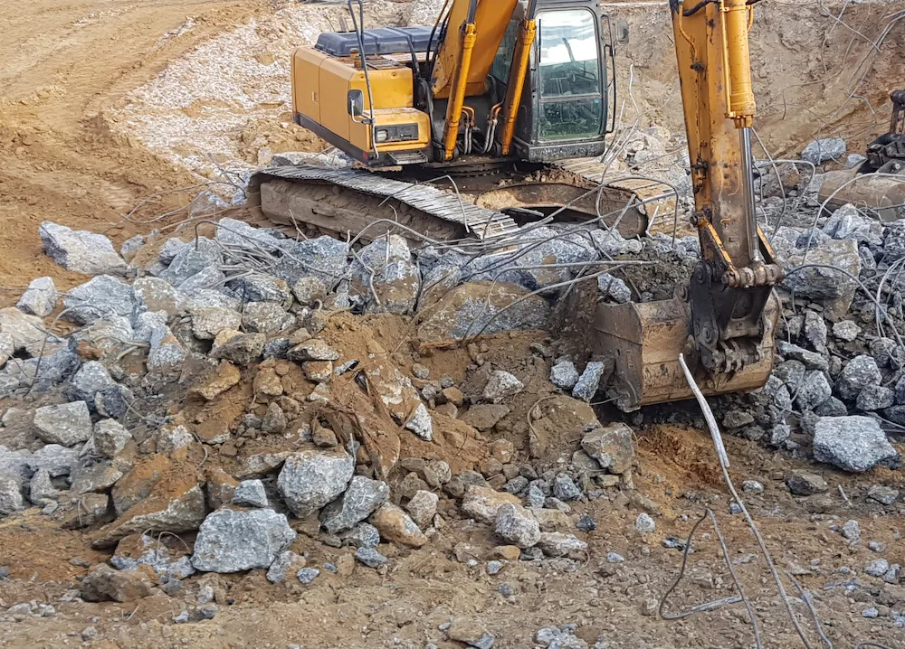 Excavator breaking up and removing concrete slabs