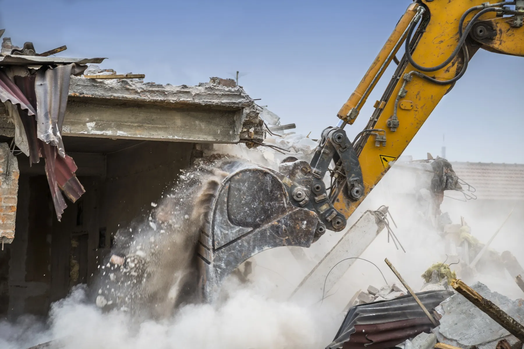 Excavator bucket demolishing a house wall in a cloud of dust