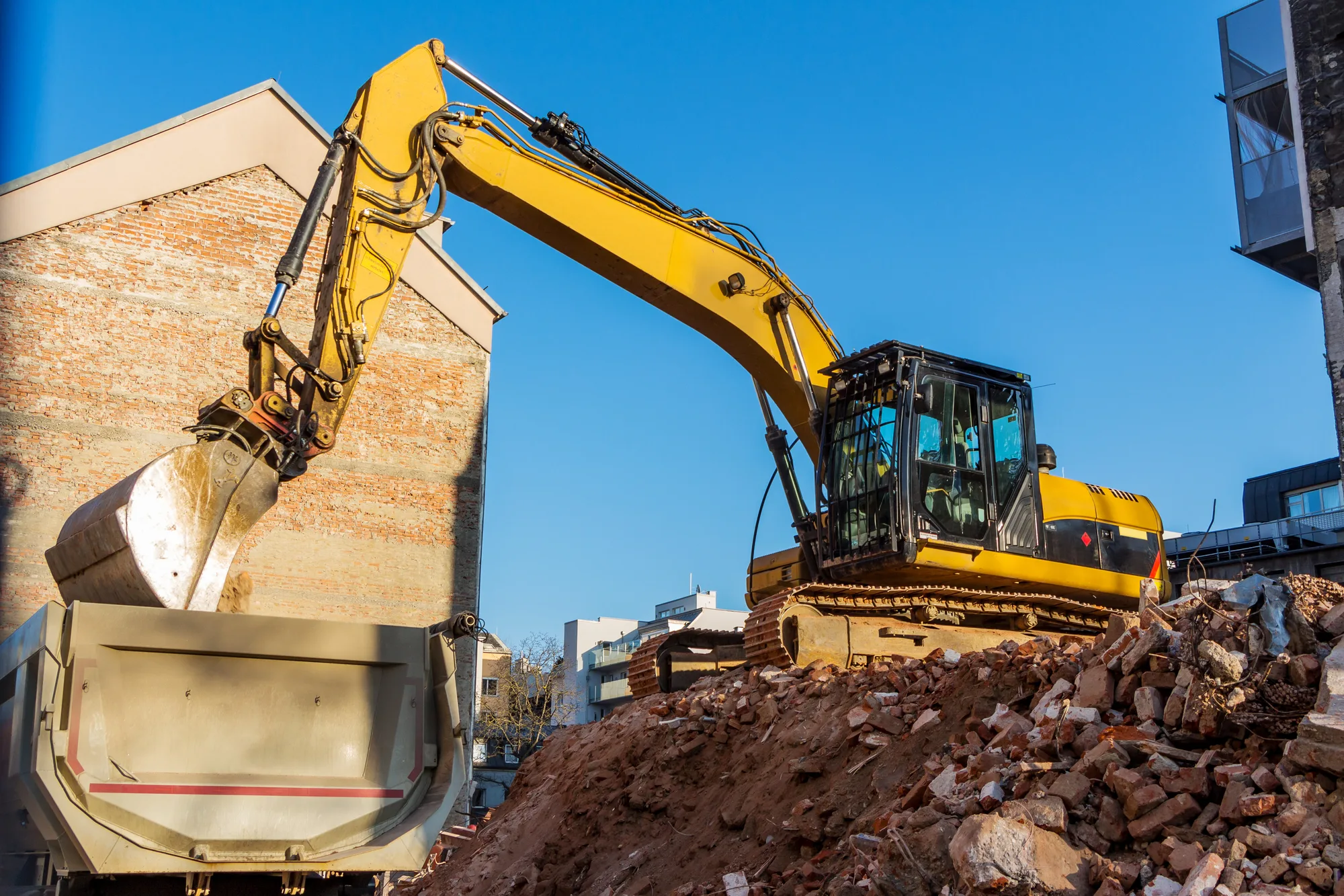 Excavator loading demolition rubble into a skip beside a building