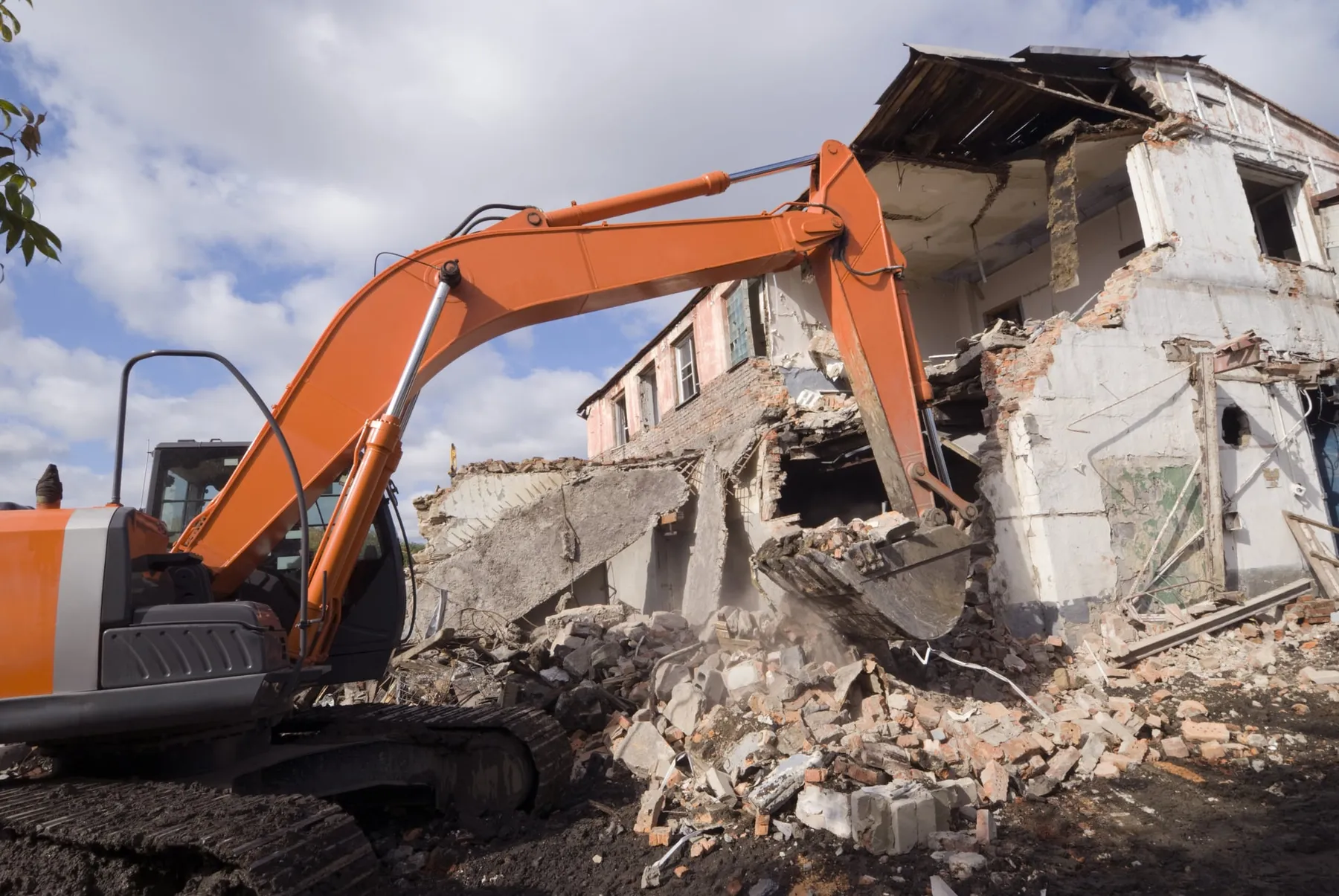Orange excavator demolishing a two-storey house